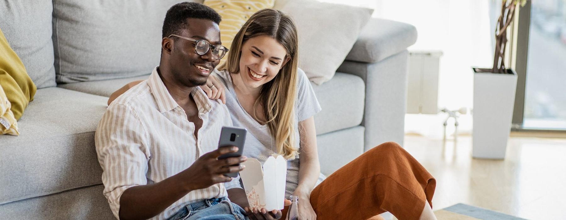 Find your perfect fit at Miller and York a man and woman with take out, sit against a couch on their living room floor and watch at their cell phone